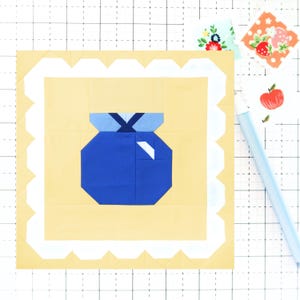 May include: A blue and white fabric applique of a blueberry with a white scalloped border on a yellow background.