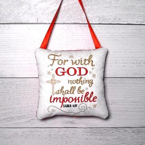 May include: A small, square, white fabric hanging ornament with a red ribbon loop. The front features embroidered text in red and gold that reads: For with GOD nothing shall be impossible LUKE 1:37, accompanied by a gold cross and star accents.