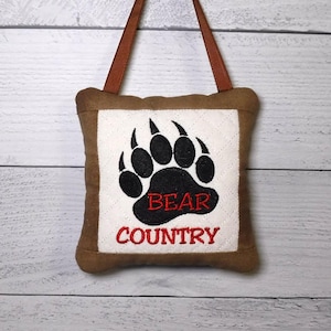 May include: A white ceramic mug with a black handle and the text "But First, Coffee" in a black, handwritten-style font. The mug is on a white surface.