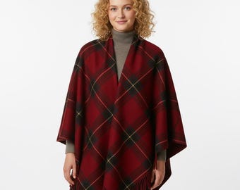 May include: A red plaid poncho with black and yellow accents and a fringed hem. The poncho is draped over a person wearing a gray turtleneck. The plaid pattern is a classic design.