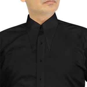 Può includere: Una camicia nera con un colletto a punta distintivo. La camicia presenta un'abbottonatura frontale con quattro bottoni visibili. Il tessuto appare liscio e ha una leggera lucentezza, suggerendo uno stile formale o elegante.