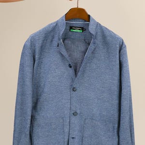 May include: A blue blazer with a mandarin collar and three buttons. The blazer has two front pockets and is hanging on a wooden hanger. The brand name "John Clothing" is visible on the label.