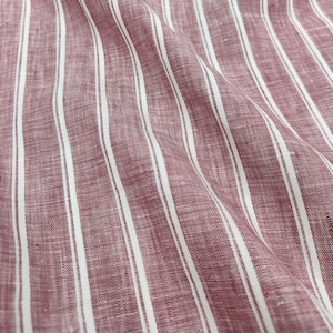 Op de afbeelding: Een stof met een patroon van verticale strepen in donkerrood en wit. Het materiaal heeft een zichtbare geweven textuur met een matte afwerking, met plooien en draperingen die diepte creëren op het oppervlak van het textielmateriaal.