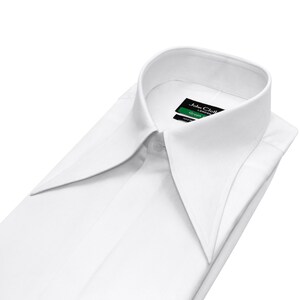 Könnte beinhalten: Ein makelloses weißes Hemd mit einem breiten Kragen. Das Hemd ist ordentlich gefaltet und zeigt sein maßgeschneidertes Design. Das Etikett lautet "John Cloth London Green". Hergestellt aus einem glatten Stoff, ideal für formelle Anlässe.