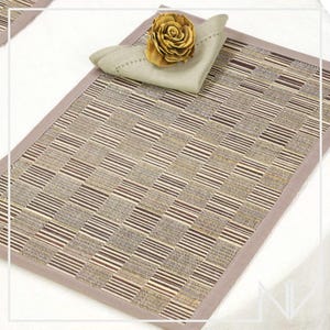 May include: A rectangular placemat with a woven pattern in shades of brown, beige, and gray, framed by a solid gray border. A folded beige napkin and a decorative flower are placed on top, creating a coordinated table setting.