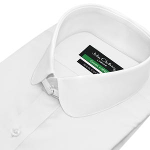 Könnte beinhalten: Ein makelloses weißes Hemd mit einem klassischen Kragen. Das Hemd hat eine Knopfleiste und ein Etikett mit der Aufschrift "John Clothier London Green Label 100% COT". Der Stoff ist wahrscheinlich Baumwolle.
