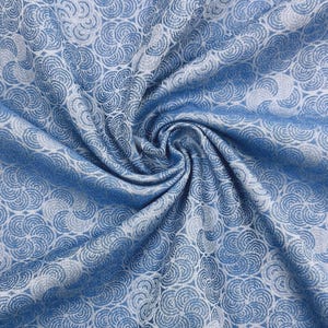 May include: A close-up of a blue and white fabric with a repeating floral pattern. The fabric is draped and folded, creating shadows and texture. The pattern consists of stylized, swirling floral motifs.