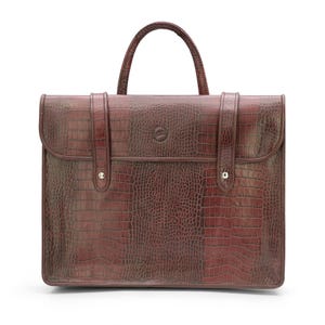 May include: A brown briefcase with a crocodile skin texture. The bag has a top handle and two straps with silver-colored button closures. A small emblem is centered on the front of the bag.