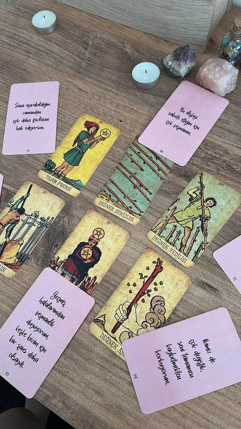 May include: A collection of tarot cards and rectangular pink message cards with Turkish text arranged on a wooden surface. The tarot cards include the Page of Pentacles, Eight of Wands, Seven of Wands, Four of Pentacles, and Ace of Wands.