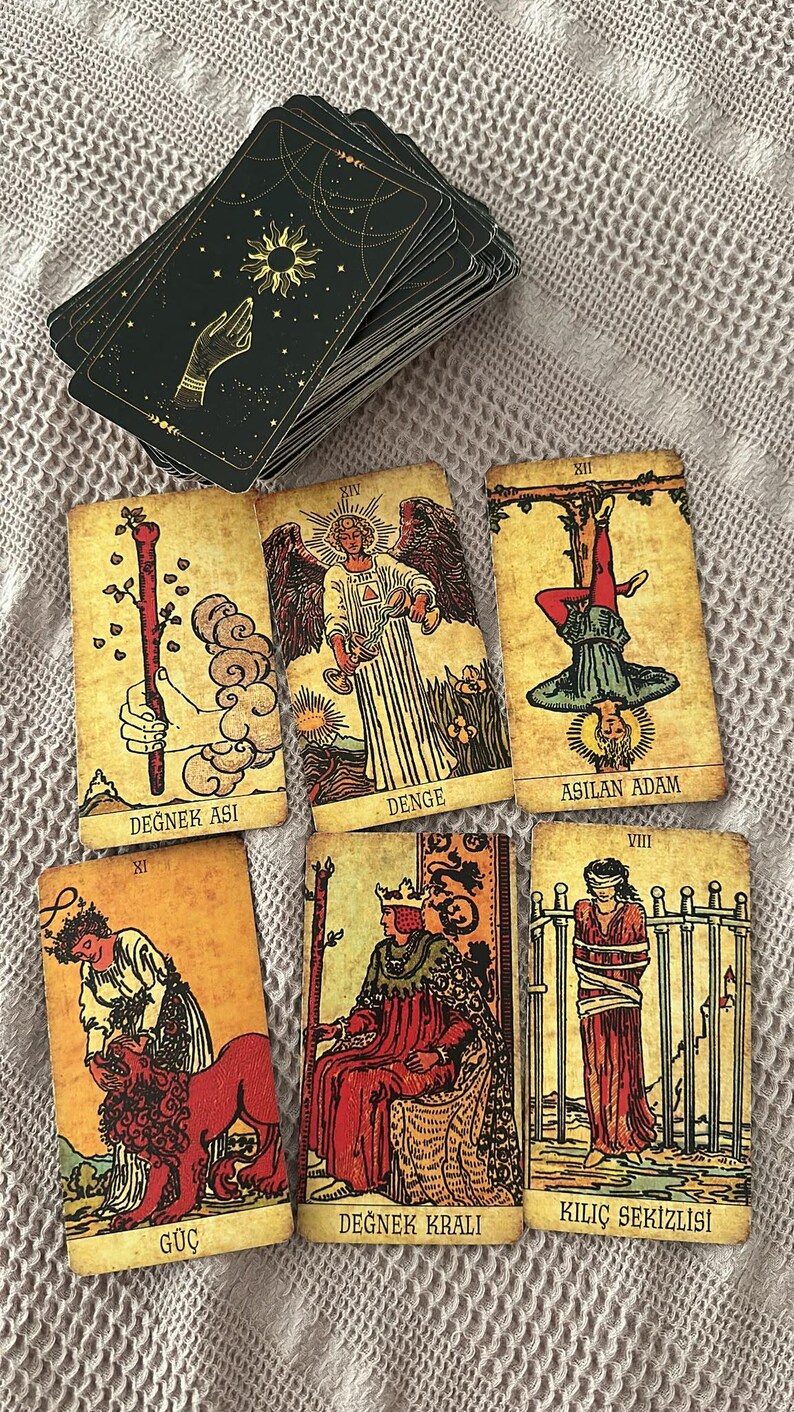 May include: A deck of tarot cards with black backs featuring a gold hand and sun design, alongside six face-up cards labelled Degnek Asi, Denge, Asilan Adam, Guc, Degnek Krali, and Kilic Sekizlisi, each displaying detailed vintage-style illustrations.