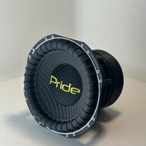 Può includere: Un subwoofer nero con la scritta "Pride" in lettere gialle. L'altoparlante ha un centro strutturato, simile alla fibra di carbonio e un bordo argentato. L'altoparlante è progettato per l'uso in un sistema audio per auto o domestico.