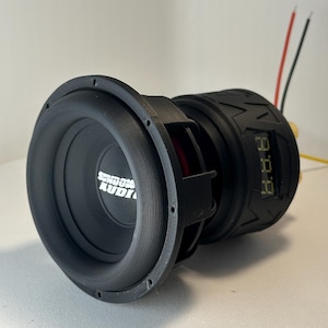 May include: A black subwoofer with the text "Sundown Audio" on the speaker cone. The subwoofer has a circular design with a black rim and a digital display on the side. Red, black, and yellow wires extend from the back.