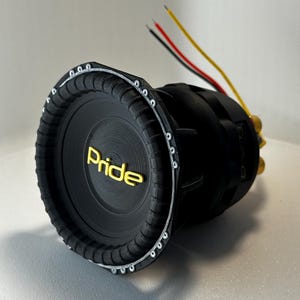 May include: A black subwoofer with the word "Pride" in gold lettering. The speaker has a ribbed edge and a series of small silver fasteners around the rim. Three wires, red, yellow, and black, extend from the back.
