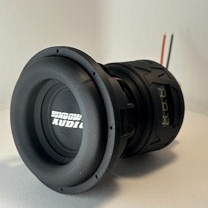 May include: A black subwoofer with the text "Sundown Audio" in white. The speaker has a circular design with a rubber surround and a digital display. Red and black wires extend from the back.