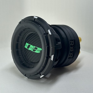 May include: A black subwoofer with a carbon fiber cone and green accents. The center of the speaker features a green logo. The side of the speaker has a digital display. The speaker is designed for car audio.
