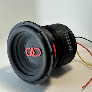 May include: A black subwoofer with a red logo and a digital display. The speaker has a circular design with a ribbed texture around the edge. Wires extend from the back of the speaker.