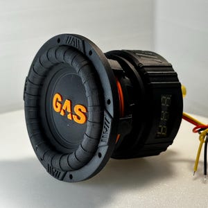 Könnte beinhalten: Ein schwarzer und orangefarbener Subwoofer mit einem digitalen Display und dem Wort "GAS" auf der Vorderseite. Der Subwoofer hat angeschlossene Kabel.