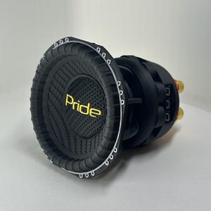Könnte beinhalten: Ein schwarzer Subwoofer mit einem Kohlefaserdesign und dem Wort "Pride" in Gelb. Der Subwoofer hat eine kreisförmige Form mit einer Reihe kleiner Löcher am Rand. Die Rückseite hat goldfarbene Anschlüsse.
