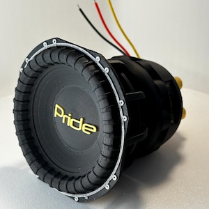 May include: A black subwoofer with the word "Pride" in gold lettering. The speaker has a ribbed edge and a silver rim with screws. Three wires, black, red, and yellow, extend from the back.