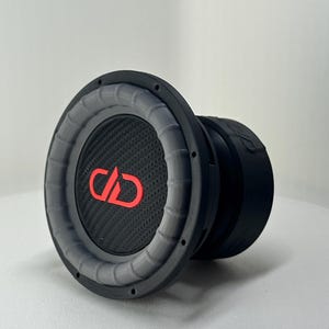 Pode incluir: Um subwoofer preto e cinza com um logotipo vermelho. O alto-falante tem um cone de fibra de carbono e uma borda cinza. O subwoofer foi projetado para uso em um sistema de áudio automotivo ou doméstico.
