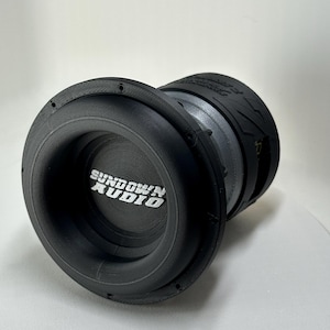May include: A black Sundown Audio subwoofer with a ribbed cone and a circular design. The brand name is printed in white on the front. The subwoofer is designed for car audio systems.