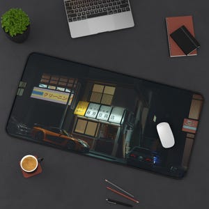 Puede incluir: Alfombrilla de escritorio rectangular negra con una escena callejera nocturna, texto japonés y un coche deportivo naranja. También se ven un portátil, un ratón y una taza de café.