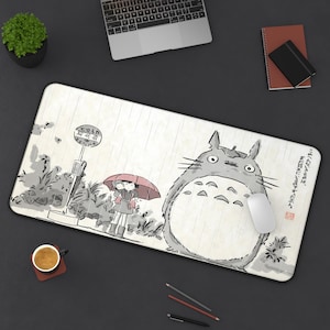 May include: A rectangular mouse pad featuring a whimsical illustration of Totoro from the animated film My Neighbor Totoro. The design includes a bus stop scene with two children under an umbrella and Japanese text. A white mouse rests on the pad.