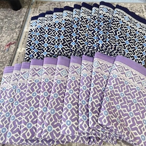 Könnte beinhalten: Eine Sammlung gefalteter Stoffe mit zwei verschiedenen Mustern. Ein Set zeigt einen marineblauen Hintergrund mit einem weißen und hellblauen geometrischen Design. Das andere Set zeigt einen lavendelfarbenen Hintergrund mit einem weißen und hellblauen geometrischen Muster.