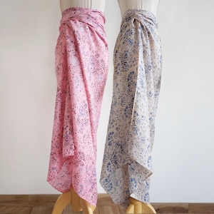 May include: Two sarongs on display. One is a soft pink with a detailed floral and bird pattern in shades of purple and grey. The other is cream with a blue floral pattern. Both are wrapped around the mannequins.