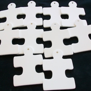 May include: Ten white ceramic puzzle pieces with a hole at the top for hanging. The pieces are arranged in a random pattern.