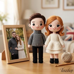 May include: A wooden framed photo of a couple stands next to two crocheted dolls, a man and a woman. The man doll wears a gray sweater and black pants. The woman doll wears a white dress and black boots. A ball of yarn and a crochet hook are also on the table.