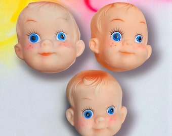 May include: Three vintage doll heads with blue eyes, rosy cheeks, and orange lips. The doll heads have light brown hair and are arranged on a white surface with a colorful background.