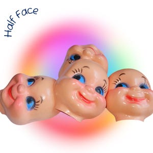 May include: A collection of vintage, smiling doll faces in a peach hue, with blue eyes and red lips. The faces are clustered together, with the text "Half Face" in blue script in the upper left corner. A rainbow gradient background adds a whimsical touch.