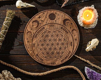 May include: A wooden divination board with a flower of life design and the words "Yes", "Maybe", "No", and "Rephrase" around the edge. The board is surrounded by various objects, including a candle, a skull, and a crystal.