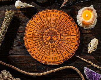 May include: An orange wooden calendar with a tree of life design at the center, surrounded by text. The image includes a lit candle, animal skulls, crystals, and rope, suggesting a spiritual or Wiccan theme.