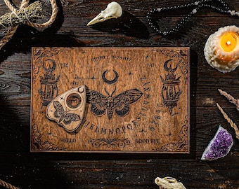 May include: A wooden spirit board featuring a moth and crescent moon design, with the alphabet, numbers, and the words "Hello" and "Good Bye". The board is surrounded by a planchette, a candle, a skull, and other mystical items.