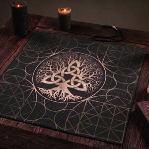 May include: A square black altar cloth featuring a central metallic gold print of a tree with intertwined roots and branches forming a triquetra knot. The background pattern consists of geometric circles and lines, creating a detailed design.