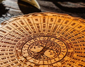 May include: A circular wooden calendar with engraved dates, months, and astrological symbols. The center features a tree design within a circle of runes. The calendar is light brown with dark brown engraved details.