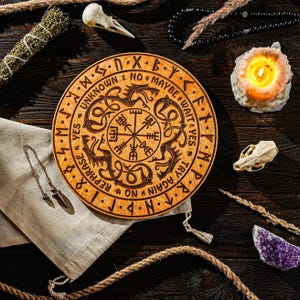 Puede incluir: Una tabla de adivinación de madera con símbolos y texto grabados, rodeada de una vela encendida, cristales y otros objetos espirituales. La tabla presenta un diseño de rosa de los vientos y las palabras "Desconocido", "Tal vez" y "Inténtalo de nuevo".