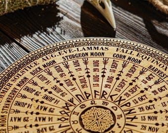 May include: A wooden circular wheel with a calendar of moon phases and names, including the Strawberry Moon, Buck Moon, Sturgeon Moon, Corn Moon, and Harvest Moon. The wheel also includes the dates of the solstices and equinoxes. The wheel is decorated with runes and Celtic knotwork.
