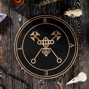 Op de afbeelding: Een zwart en goud houten zegel met de letters B, A, L en E langs de rand. De afbeelding bevat kaarsen, kristallen en een vogel schedel, wat een mystieke esthetiek creëert.