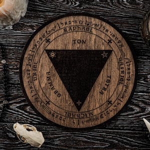 May include: A round wooden sigil with a dark triangle at the center, surrounded by text and symbols. The sigil is brown with a dark brown triangle. The image includes candles, a rosary, and a skull.