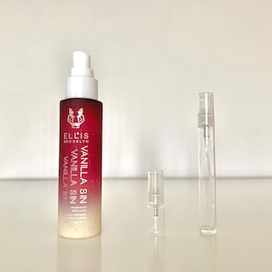 May include: A red and white bottle of Ellis Brooklyn Vanilla Sin fragrance with a white spray nozzle. The bottle is sitting on a white surface next to two clear glass spray bottles.