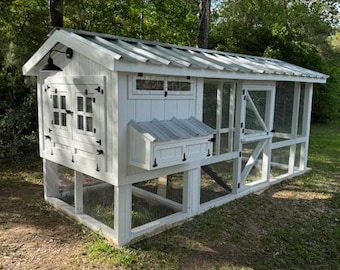 May include: White chicken coop with a metal roof, a nesting box, and a large run. The coop has a window and a door. The run is enclosed with wire mesh.