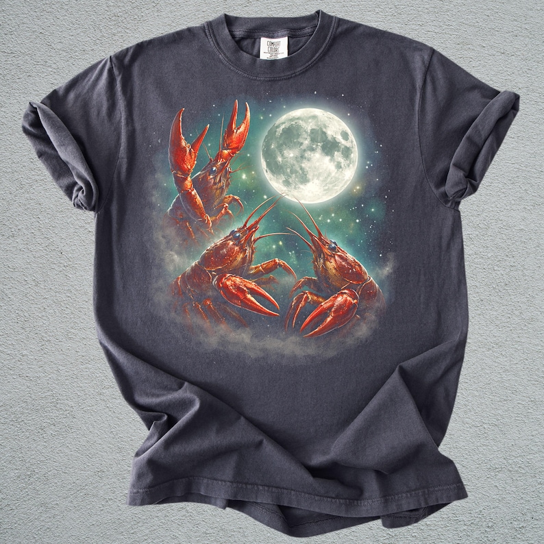 K&ouml;nnte beinhalten: Dunkelgraues T-Shirt mit einer Illustration von drei roten Krebsen vor einem Vollmond und einem Sternenhimmel. Das T-Shirt hat einen Rundhalsausschnitt und kurze &Auml;rmel. Das Design ist detailliert.