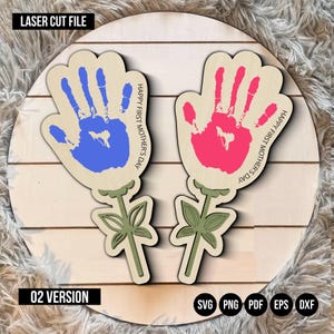 Könnte beinhalten: Zwei lasergeschnittene Holzhandabdruckblumen mit grünen Stielen und Blättern. Die Handabdrücke sind blau und rosa und der Text "Happy First Mother's Day" ist auf jeder Blume geschrieben.