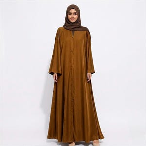 May include: A floor-length, solid brown abaya featuring long, wide sleeves and a front button-down closure. The garment is paired with a matching brown hijab that covers the head and neck, creating a cohesive, monochromatic ensemble.