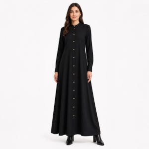 以下が含まれることがあります： 長袖でスタンドカラーの床まで届く長さの黒いドレス。この衣服は、ネックラインから裾まで伸びる小さな明るい色のボタンが付いたフルレングスのフロントボタン留めが特徴で、構造的でしっかりとしたシルエットを作り出しています。
