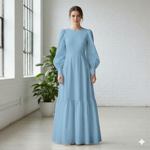 May include: A floor-length light blue dress featuring long, voluminous puff sleeves with fitted cuffs, a round neckline, and a tiered skirt design. The garment has a structured bodice that transitions into a full, flowing skirt that reaches the floor.