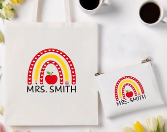 May include: A white tote bag and a small pouch with a rainbow design, a red apple, a pencil, and the text "MRS. SMITH". The rainbow has red hearts, yellow and red arches. Two white coffee cups are visible.
